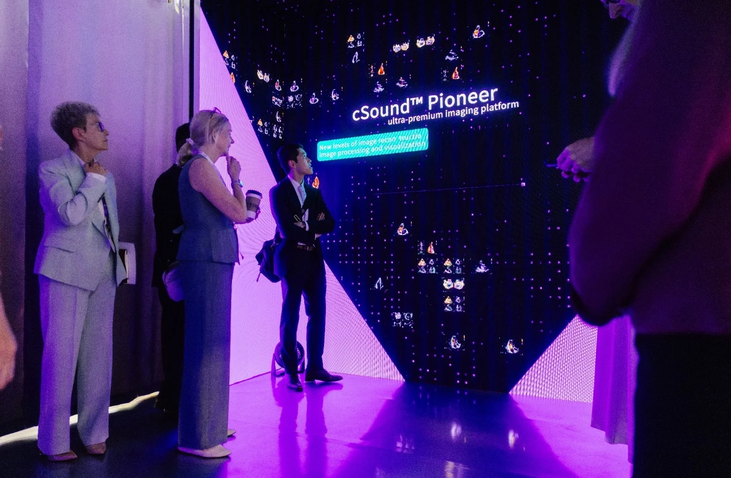 Conference attendees viewing a large branded exhibit display lit in dramatic purple lighting