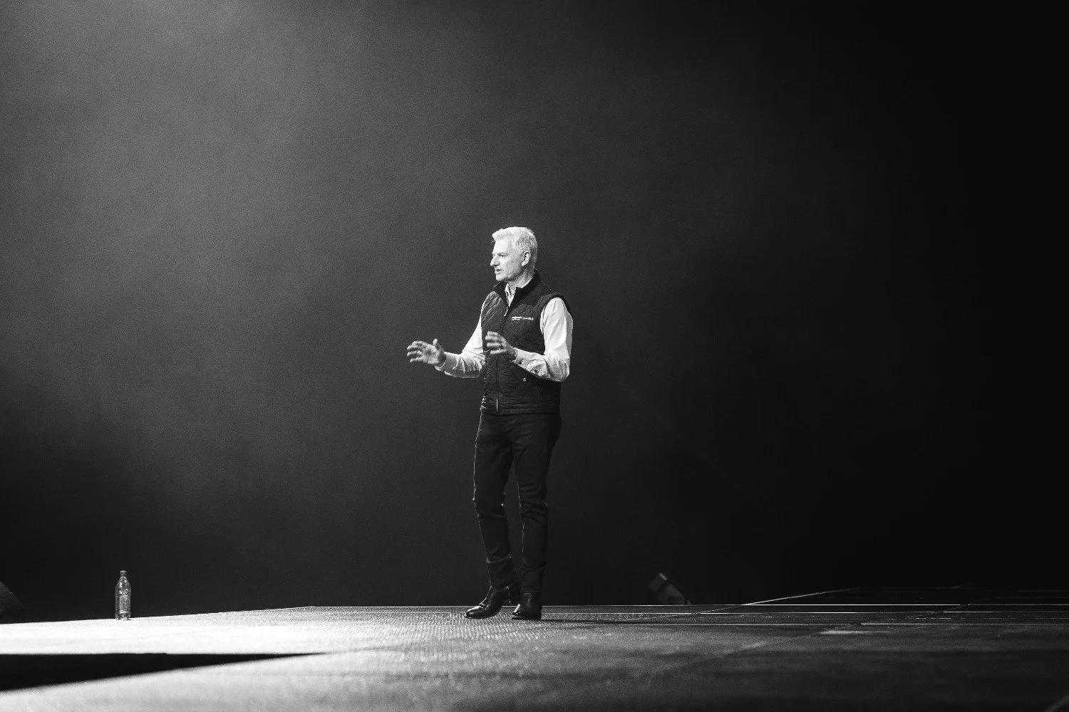 Speaker gesturing on a dramatically lit stage in black and white during a Nashville conference