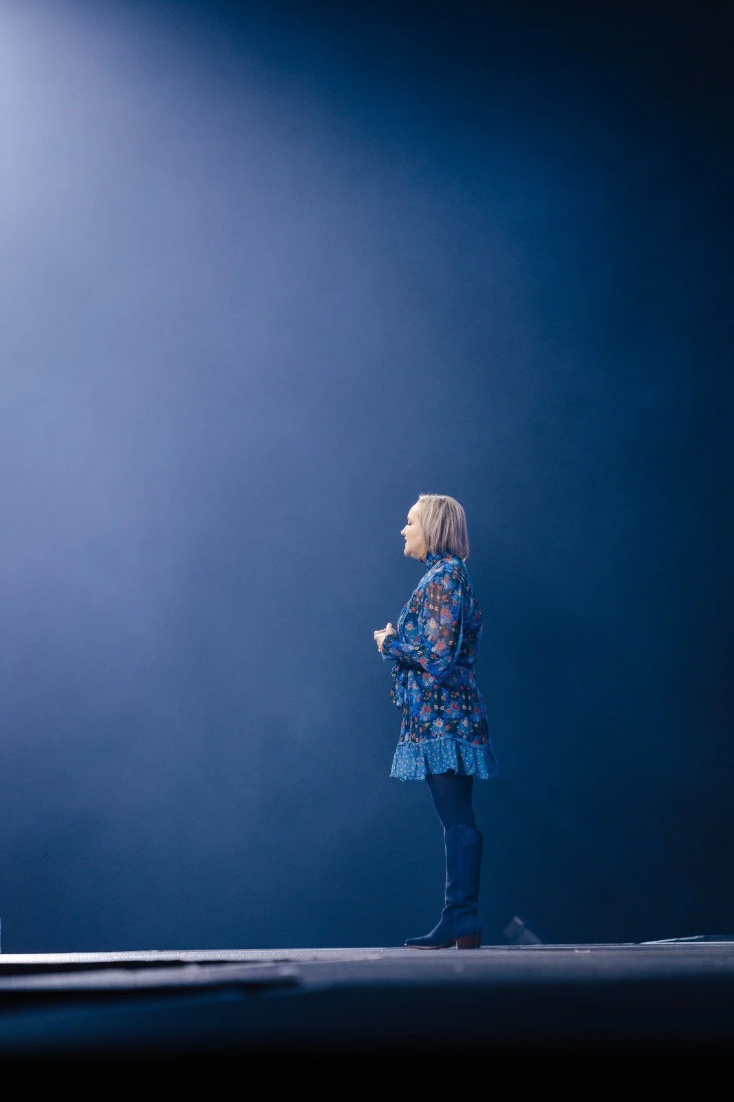 Silhouette of a speaker standing under a single blue spotlight on a Nashville conference stage
