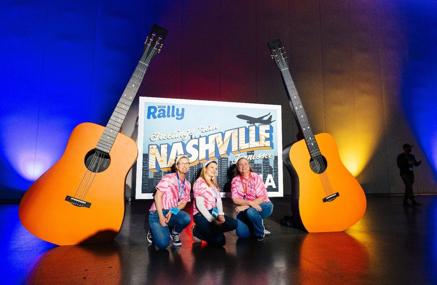 Attendees posing with oversized guitar props beside a 'Greetings from Nashville' sign at a conference photo activation