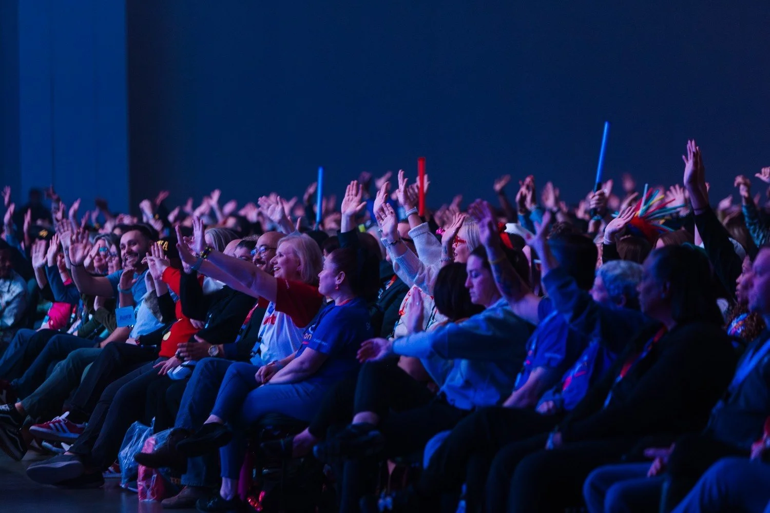 Excited conference crowd raising hands with glow sticks at a Nashville event