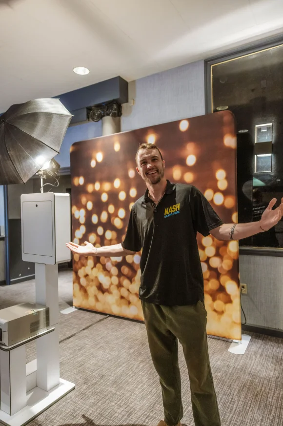 Nash Creative House crew member standing beside a headshot booth kiosk with a branded lit backdrop panel