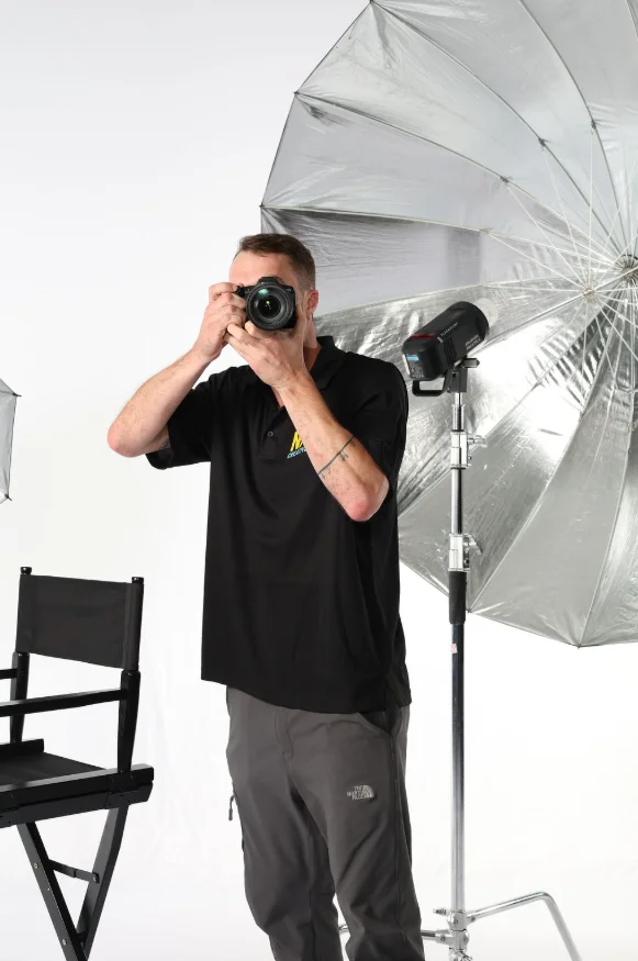 Nash Creative House photographer holding a camera up to shoot in front of a studio lighting umbrella