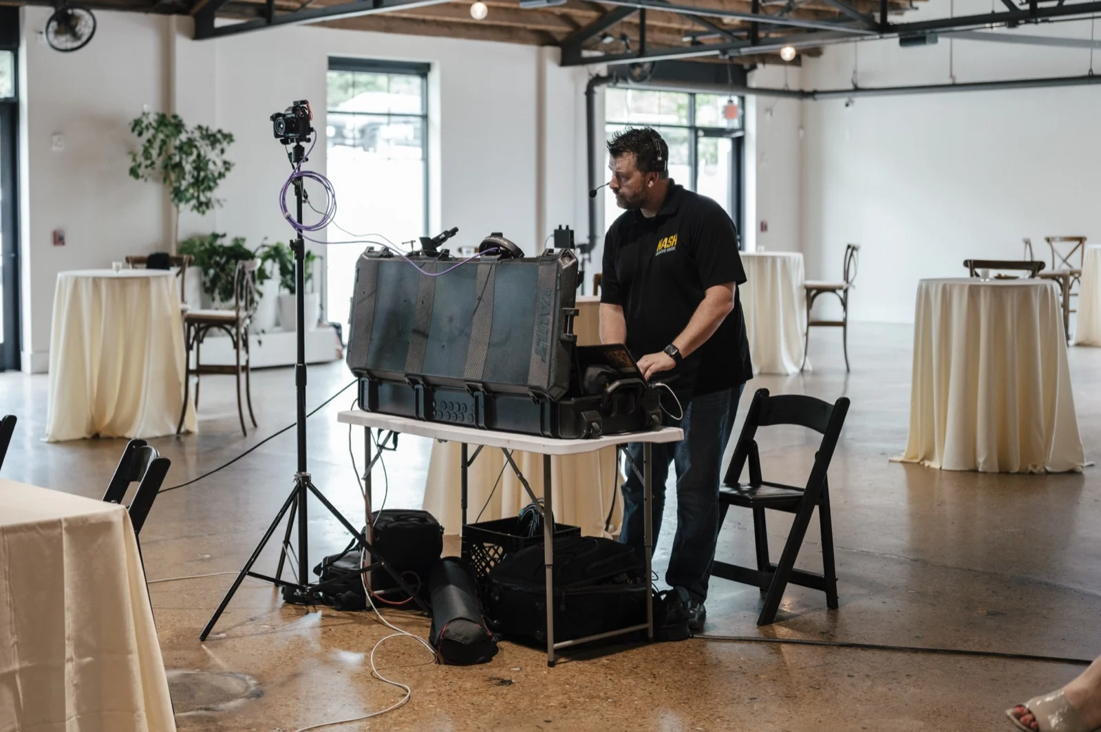 Production crew setting up multi-camera switching gear on a table in an empty event room