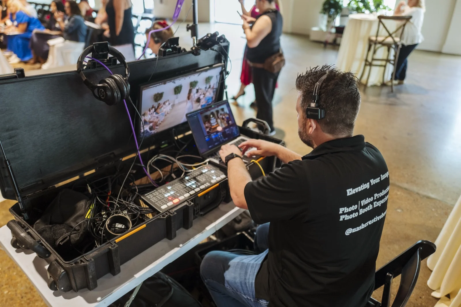 Production crew member operating a multi-camera switching station with dual monitors at a corporate event