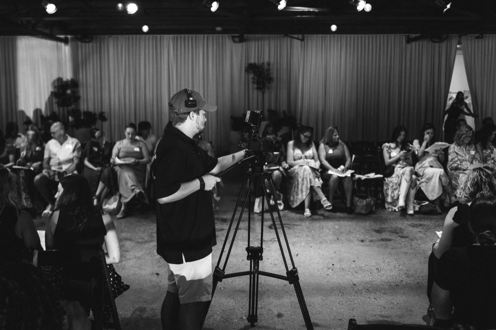 Black and white photo of a cameraman filming a seated business panel discussion